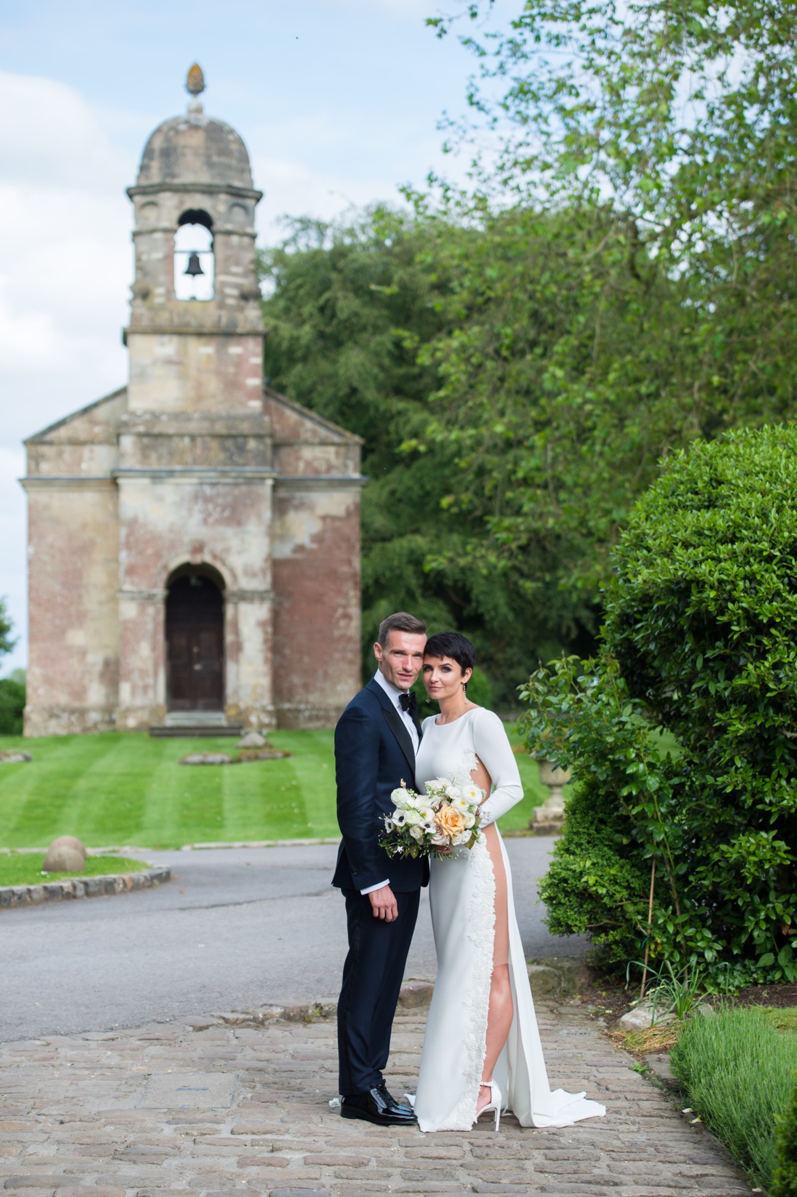 a bride and groom standing outside the chapel at babington house